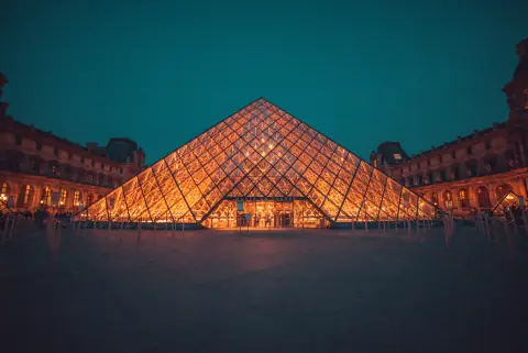 Pyramide du Louvre éclairée, encadrée par les façades du palais à la nuit tombée