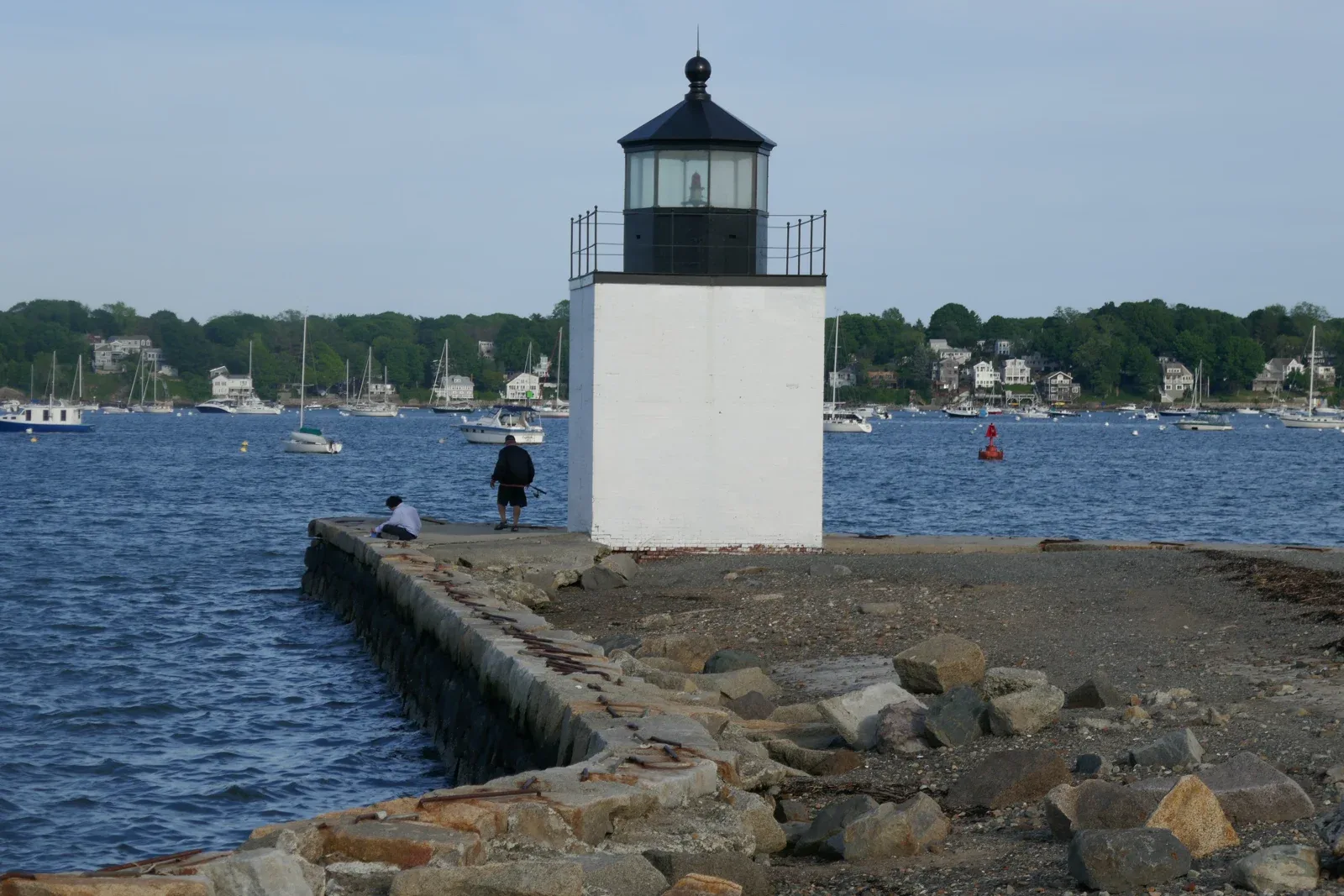 Faro blanco de Derby Wharf, con el puerto y los barcos de Salem al fondo.