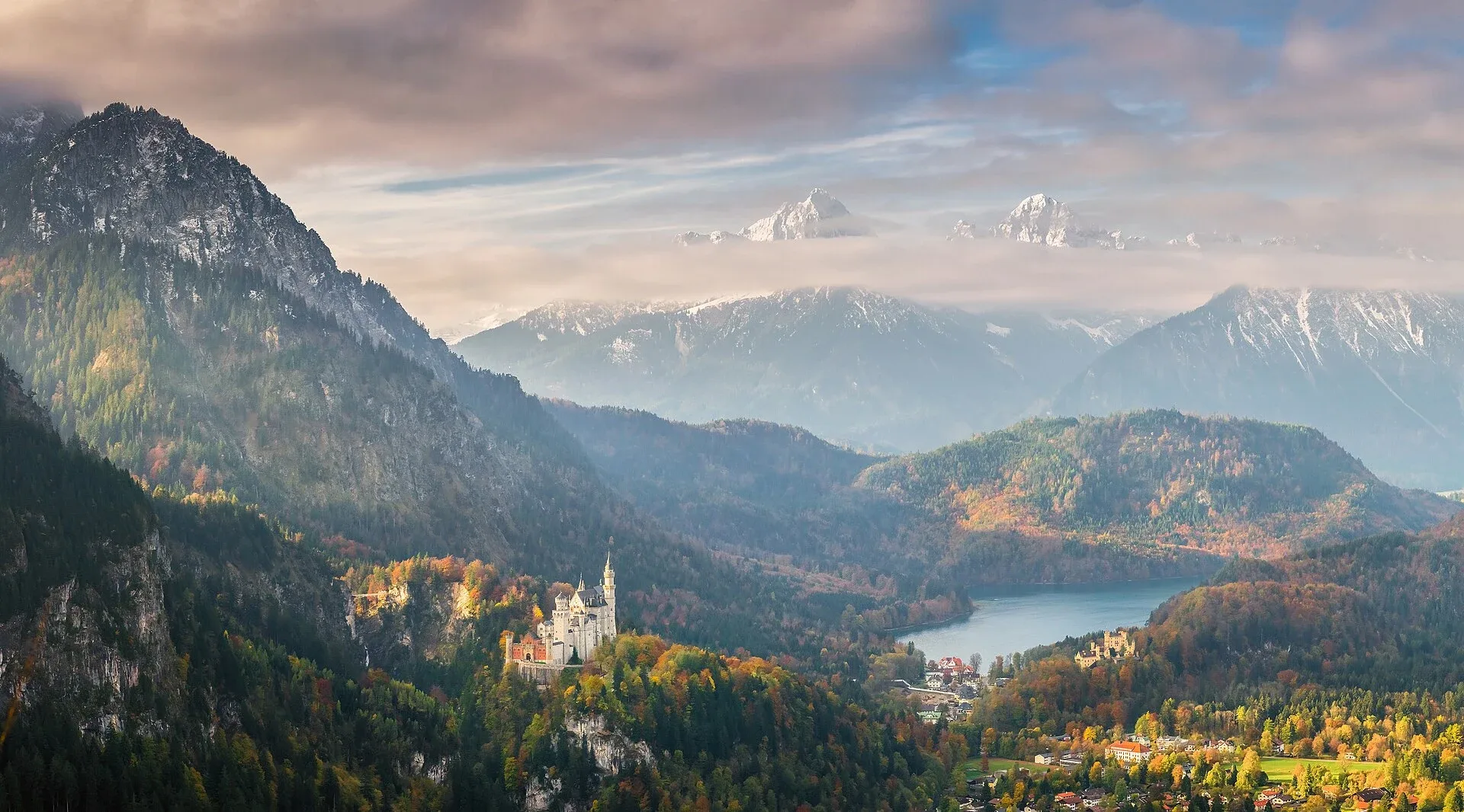 Neuschwanstein til venstre, Hohenschwangau til høyre og innsjøen Alpsee i et høstlandskap dominert av fjell.