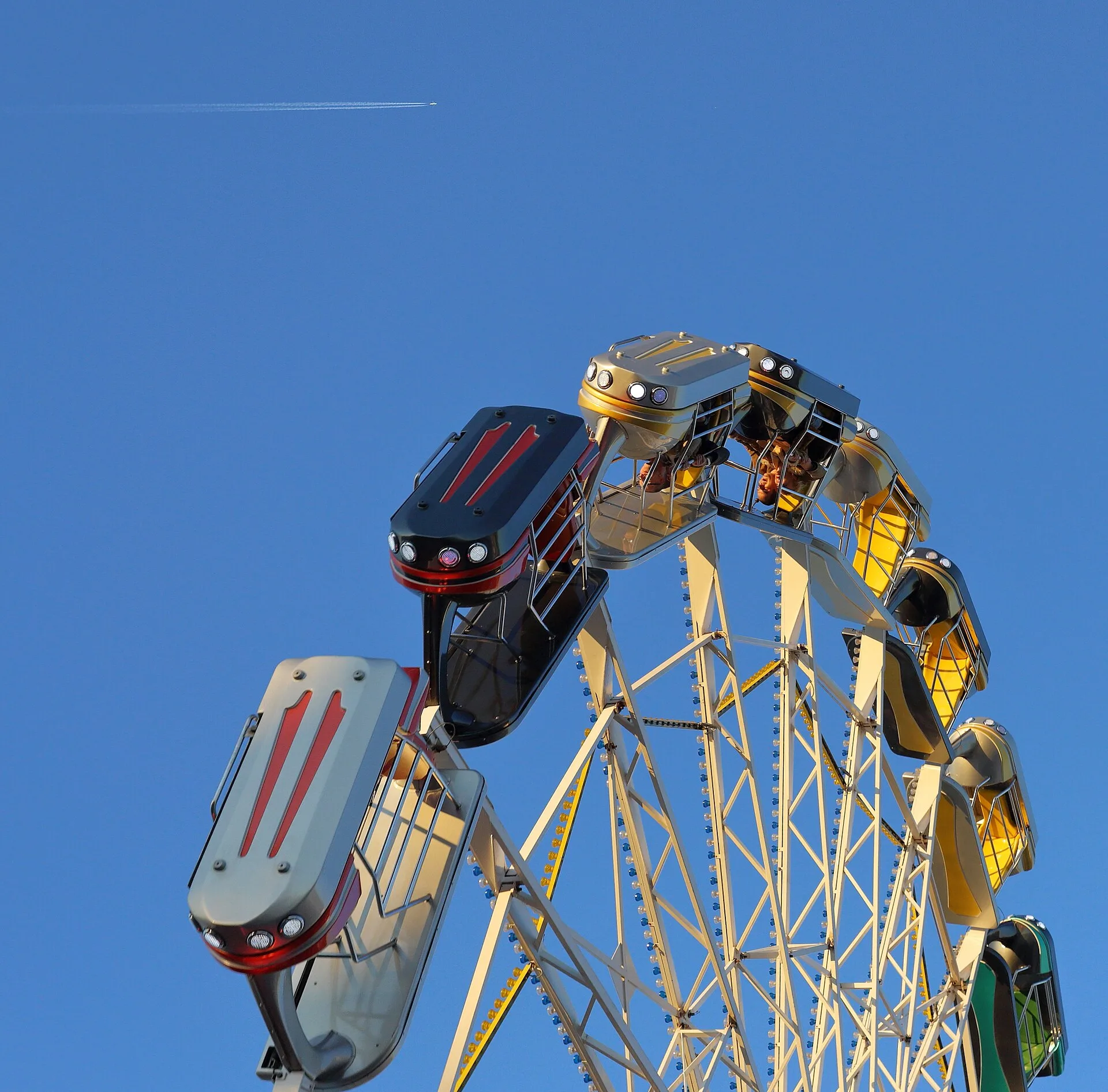 Die Gondeln eines Fahrgeschäfts neigen sich über dessen Metallkonstruktion vor blauem Himmel.